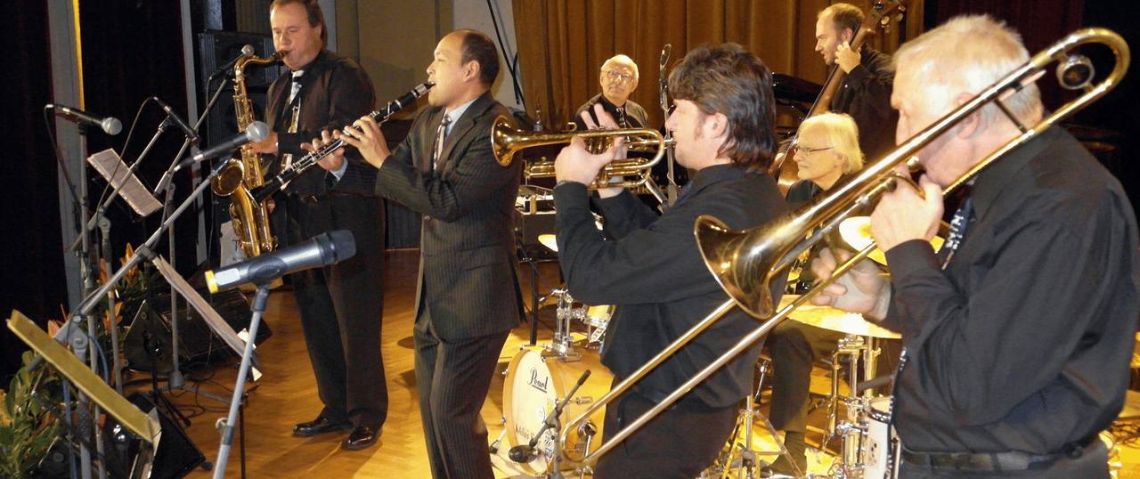 J.J. Jazzmen s hostem Evanem Christopherem z New Orleans na pódiu, v popředí pozoun.