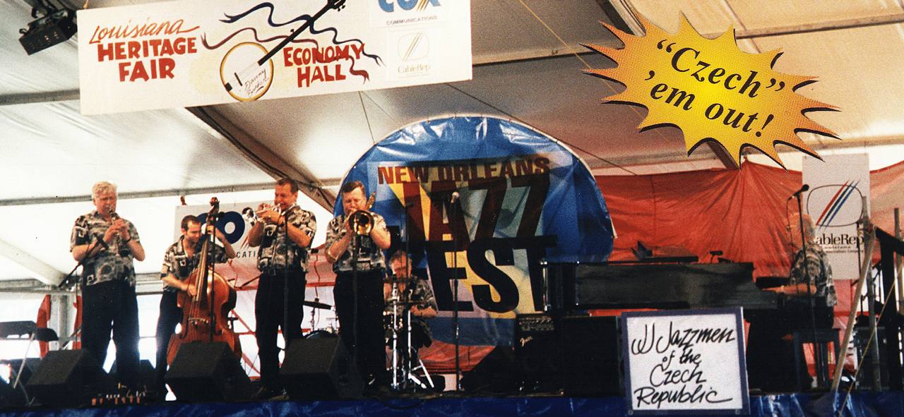 Kapela na pódiu pod stanem festivalu New Orleans Jazz Fest, vpředu cedule J.J. Jazzmen of the Czech Republic.